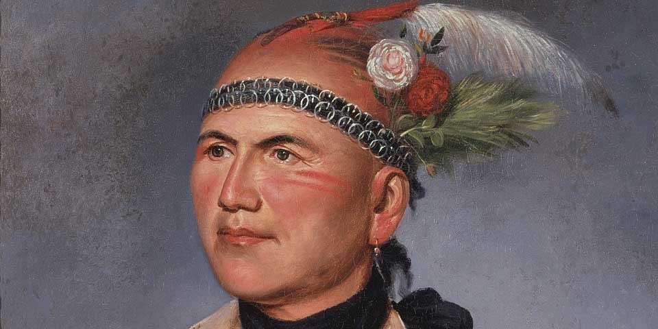 Color image of a detail of a painting of Joseph Brant/Thayendanegea, showing his face. His black hair is in a scalp lock decorated with feathers and flowers, and he wears a black headband with silver rings. Color image of a detail of a painting of Joseph Brant/Thayendanegea, showing his face. His black hair is in a scalp lock decorated with feathers and flowers, and he wears a black headband with silver rings.