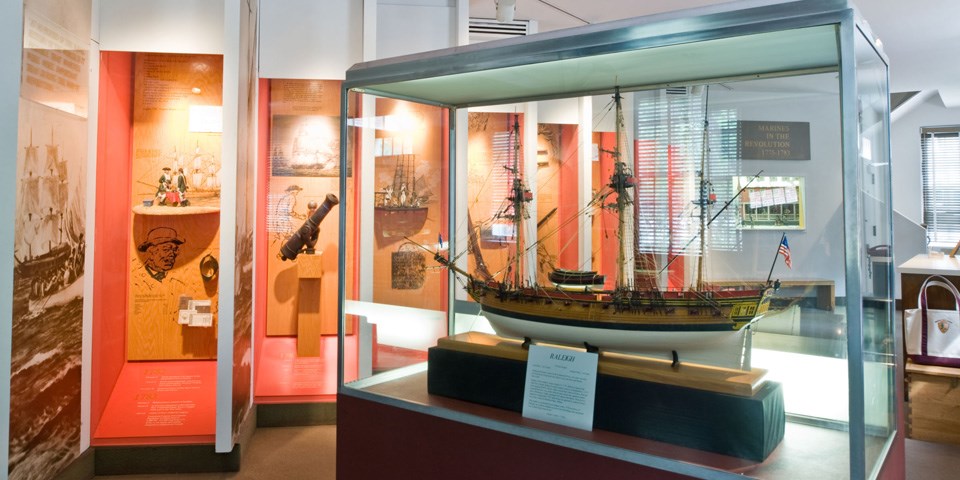 Color photo of exhibit area with ship model in case in foreground.