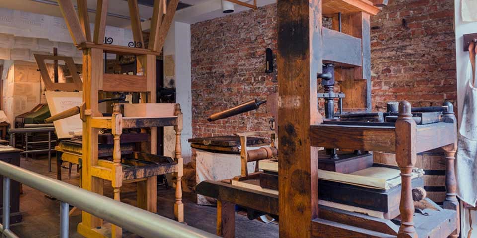 Color photo of two reproduction 18th century printing presses made mainly of wood.