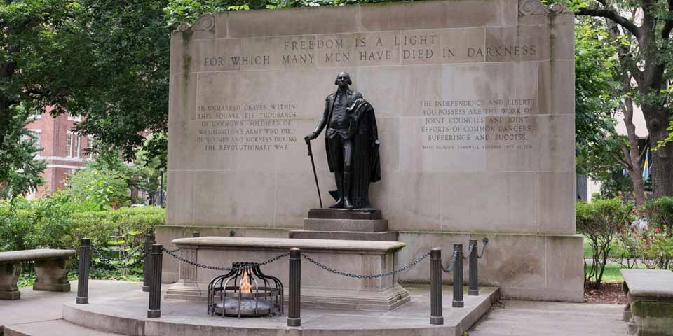 Color photo of statue of George Washington on plinth in front of tomb and eternal flame. Behind Washington is a wall with text reading "Freedom is a light for which many men have died in darkness." Color photo of statue of George Washington on plinth in front of tomb and eternal flame. Behind Washington is a wall with text reading "Freedom is a light for which many men have died in darkness."