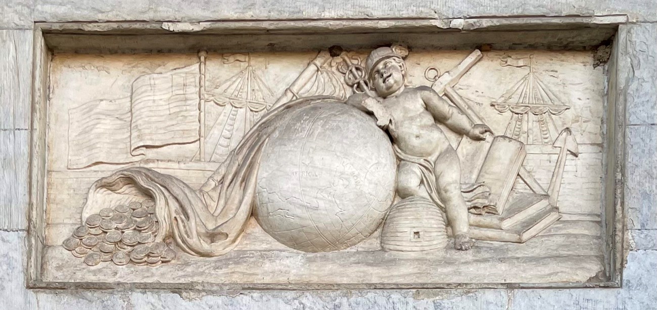 Carved stone allegory represents early American economy with a baby, American flag, books, ships, globe, and a beehive.