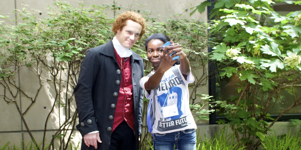 Color image of a man dressed in colonial garb posing for a selfie with a teen girl.