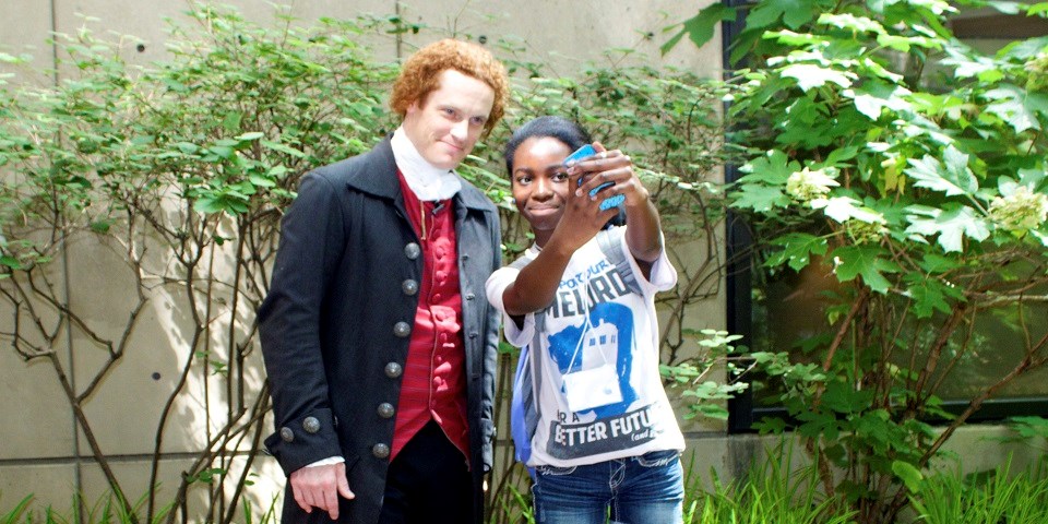 Color image of a man dressed in colonial garb posing for a selfie with and a teen girl.