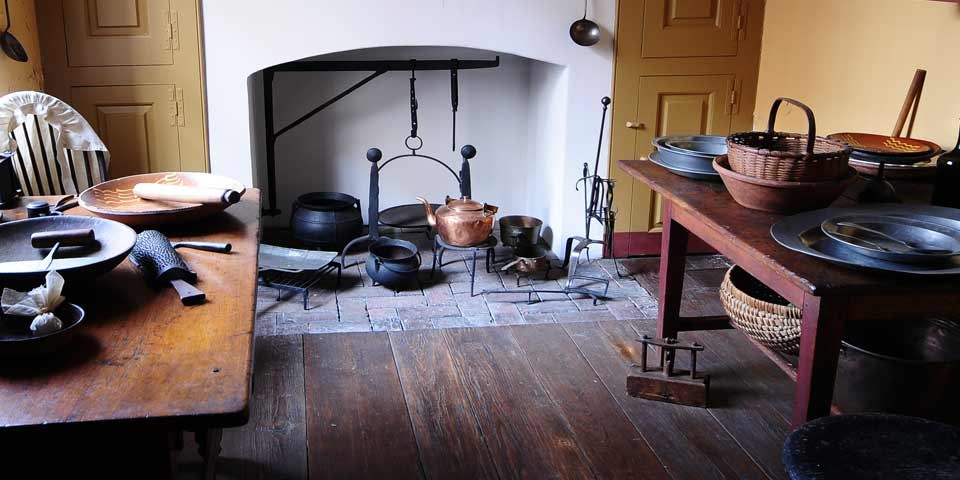 Color photo of a kitchen with two work tables, and an open hearth.