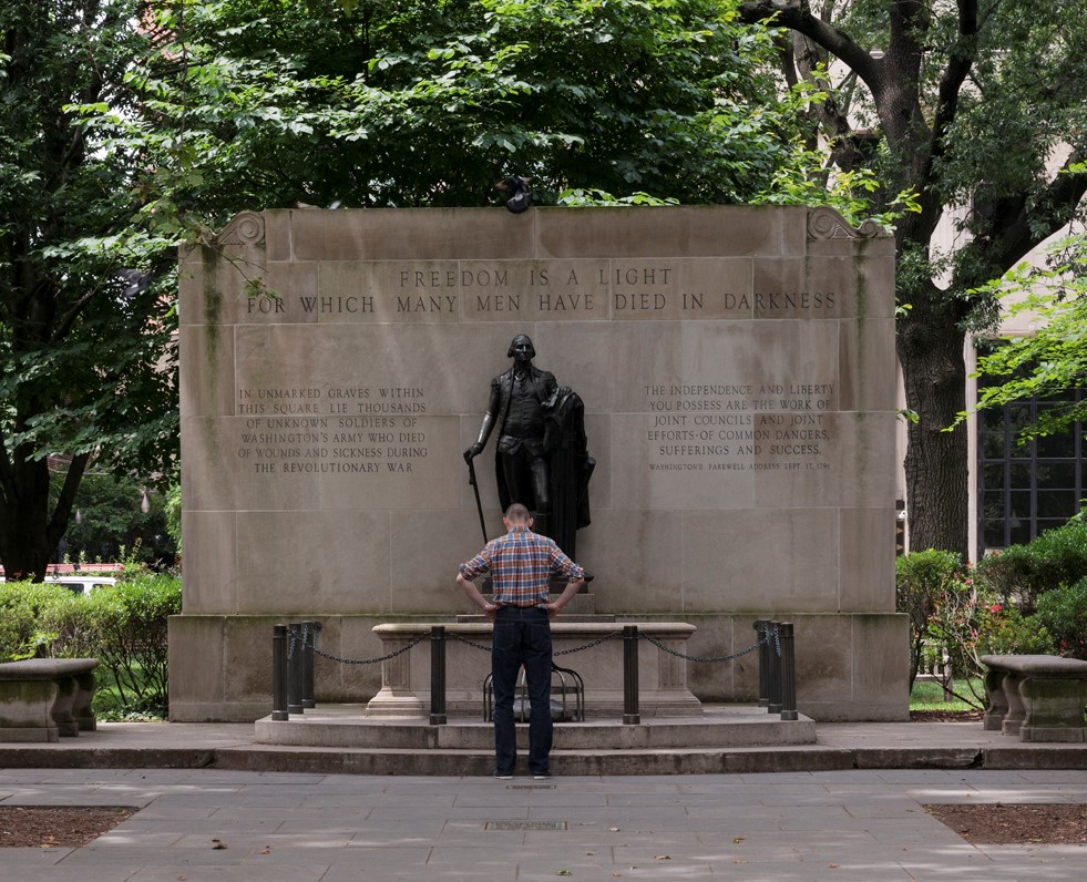 A park visitor stands in front of the Tomb of the Unknown Soldier in Washington Square with trees in the background