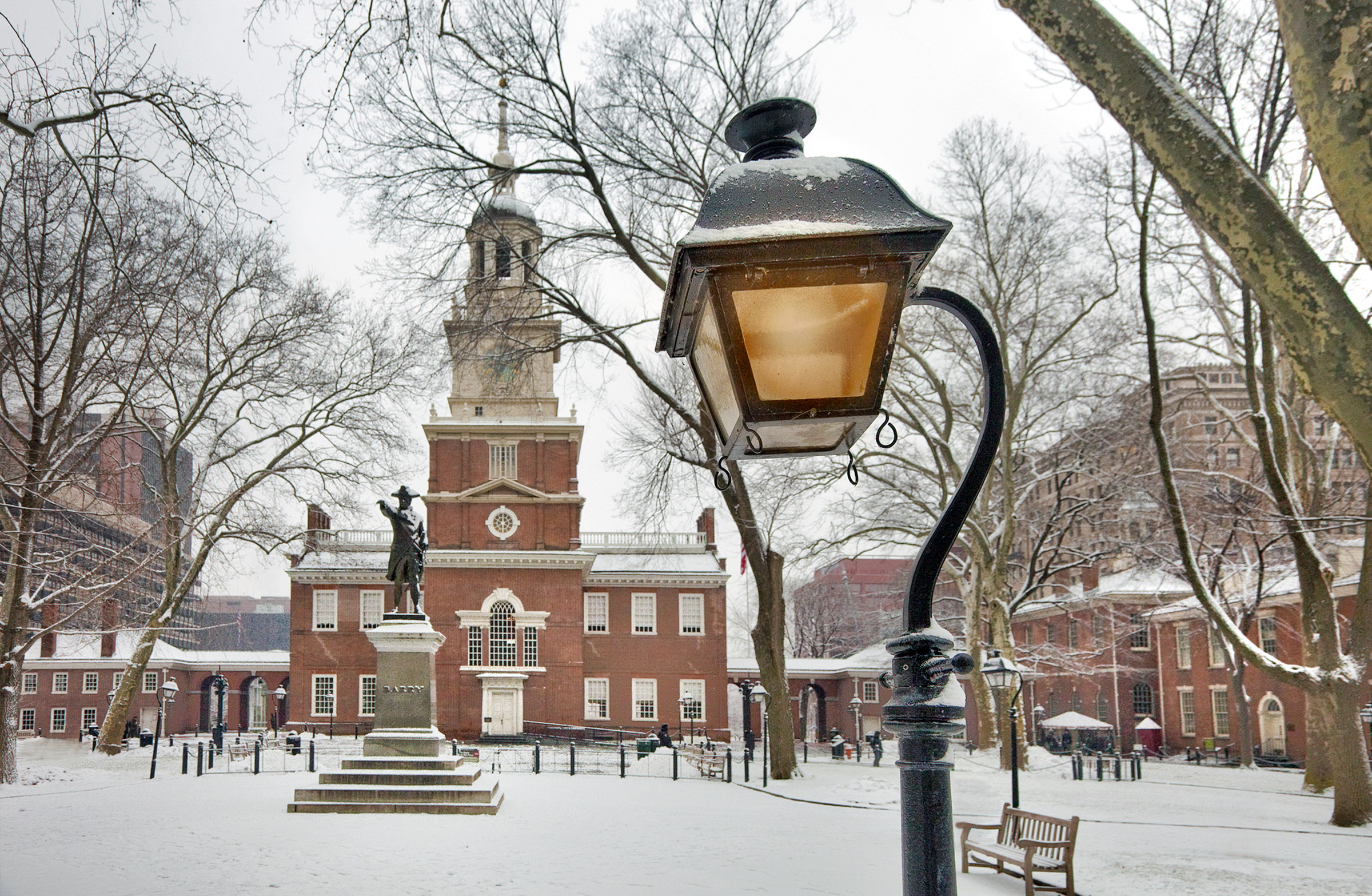 Independence Hall in the snow Brick building with clock tower and a statue in front, snow covered