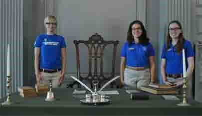 Student Conservation Association Interns, wearing blue shirts, stand next to the Rising Sun Chair. Table with green cloth is in front of them. On the table sits a replica of the inkstand used to sign the Declaration of Independence. Student Conservation Association Interns, wearing blue shirts, stand next to the Rising Sun Chair. Table with green cloth is in front of them. On the table sits a replica of the inkstand used to sign the Declaration of Independence.