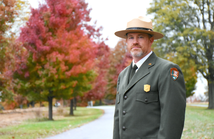A person wearing an NPS uniform with jacket and flat hat.