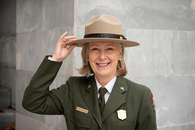 Superintendent Cindy MacLeod A person wearing NPS green and gray uniform with hand on flat hat.