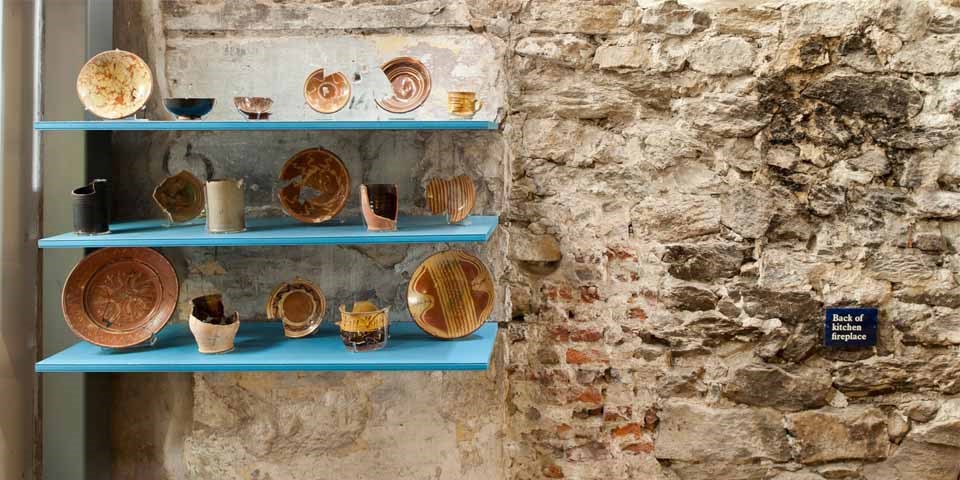 Color photo of pottery fragments on a display shelf set in an exposed brick wall in the Fragments of Franklin Court Exhibit.