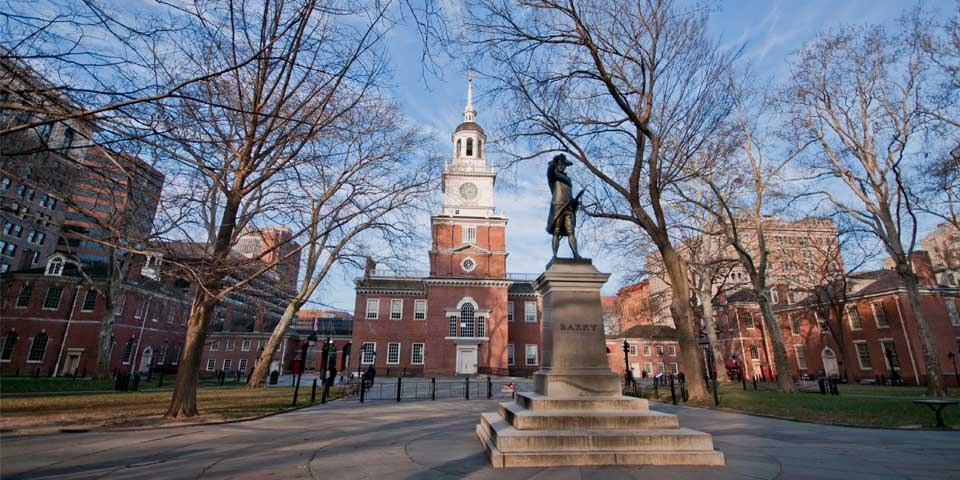 Color photo of Independence Square, showing a statue of John Barry in the foreground and a row of brick buildings in the background.