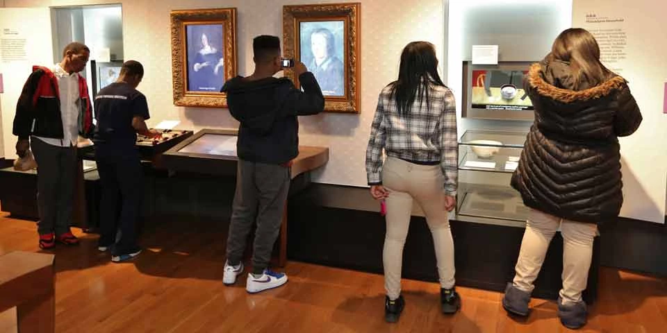 Teens viewing exhibits in the Benjamin Franklin Museum Color photo of five teens with their backs to the camera, looking at the exhibits in the Benjamin Franklin Museum