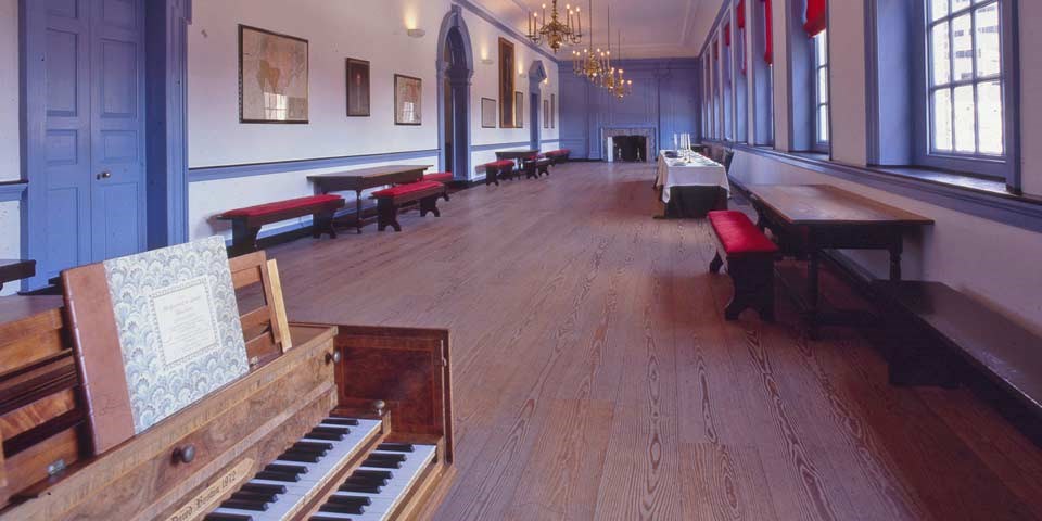 Color photo of a long, wood-floored room with a harpsichord in the foreground and benches lining the walls. Color photo of a long, wood-floored room with a harpsichord in the foreground and benches lining the walls.