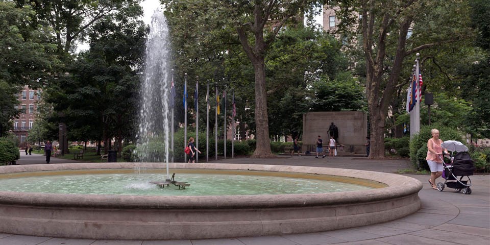 Color photo of Washington Square fountain, a low circular fountain with a plume of water rising from the center.