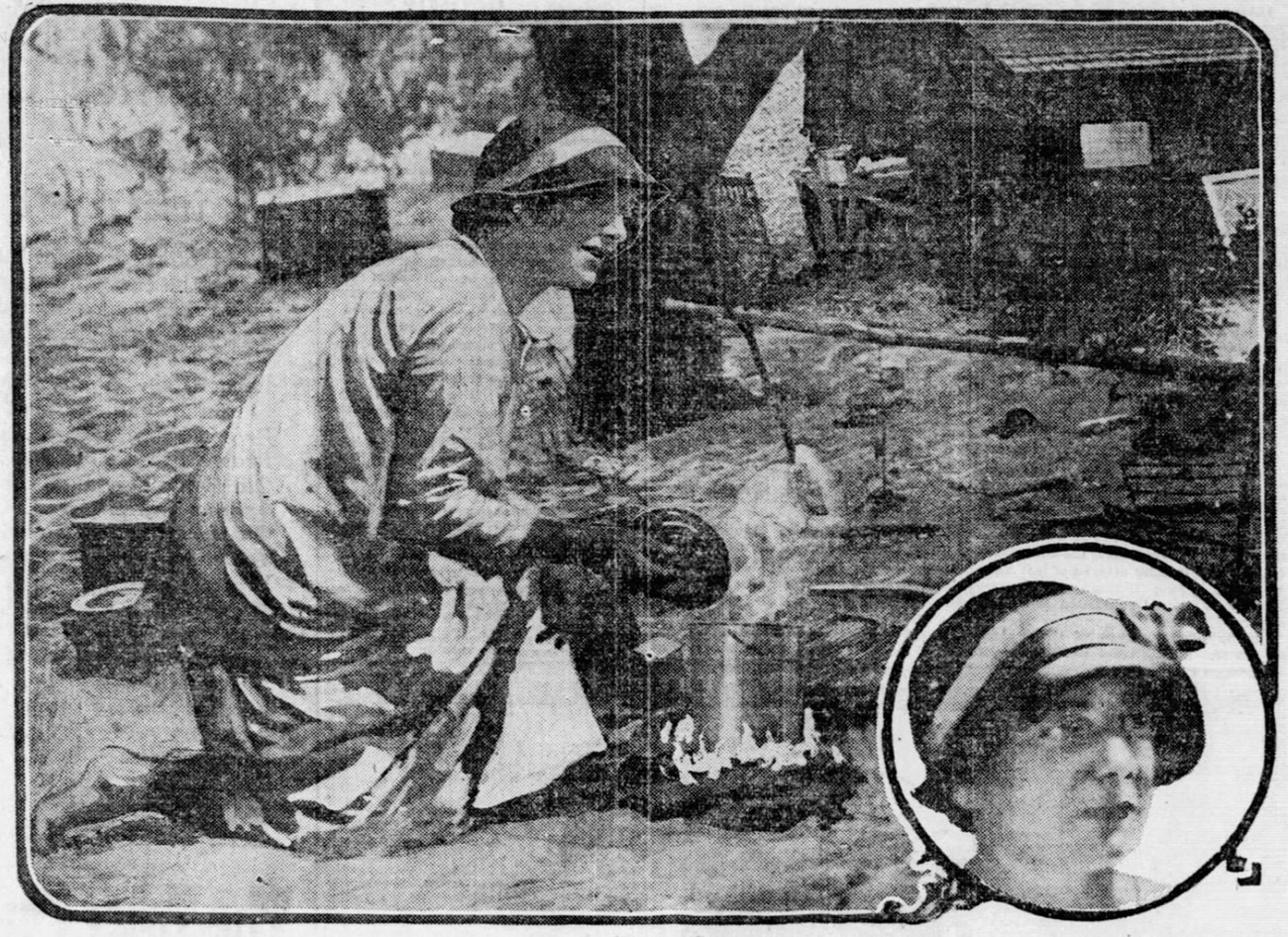 Alice Gray Black and white photograph of a woman wearing a long, light-colored garment and a hat. She is bent over a campfire, tending to a pot on the flames. Sand, trees, and wooden structures are seen in the background.