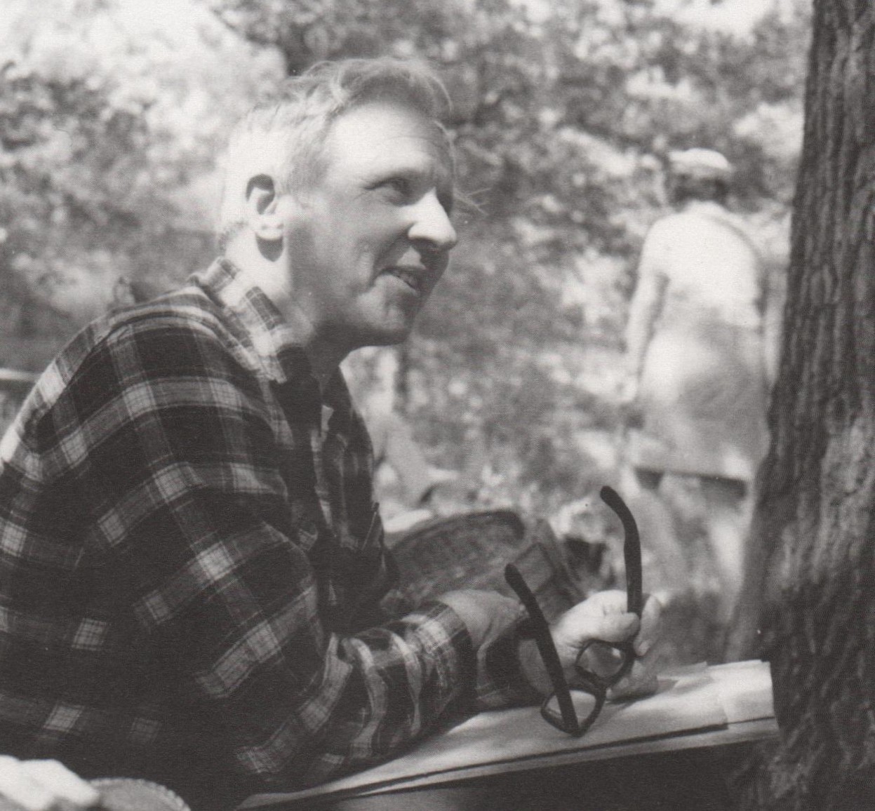 White-haired man half-smiling while seated near an oak tree.
