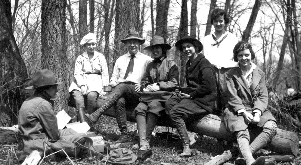 Black and white photograph of Henry Cowles seated on a downed log with 6 students in a woods