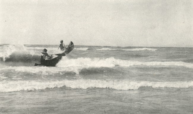 Two canoeists charge through breakers coming onto the shore of Lake Michigan