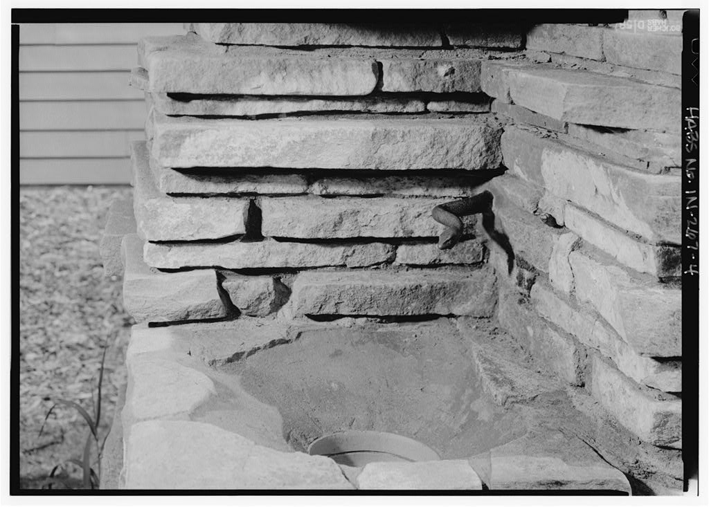 Historic black and white photograph. Close up view of the drinking area of a memorial fountain built of stone by Jens Jensen.  A bronze snake emerges from the corner.