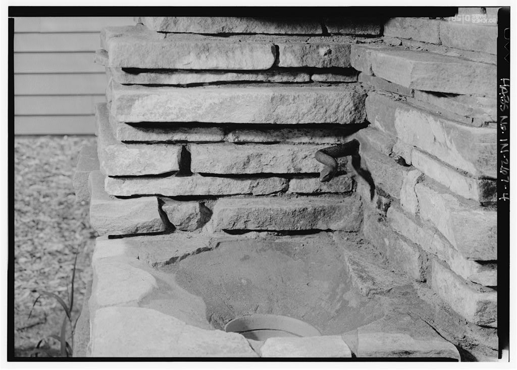 Historic black and white photograph. Close up view of the drinking area of a memorial fountain built of stone by Jens Jensen.  A bronze snake emerges from the corner.