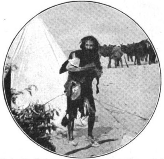 Black and white photograph of an actor dressed as a wild man with unkempt hair and ragged clothes