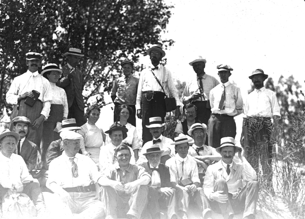 Henry Cowles and a group of over twenty others sit and stand in the Indiana Dunes