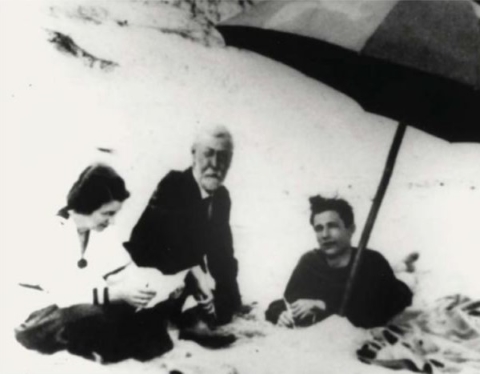 Henry Blake Fuller at Top o' Dune A white haired gentleman sits with a younger man and a younger woman underneath a beach umbrella surrounded by sand