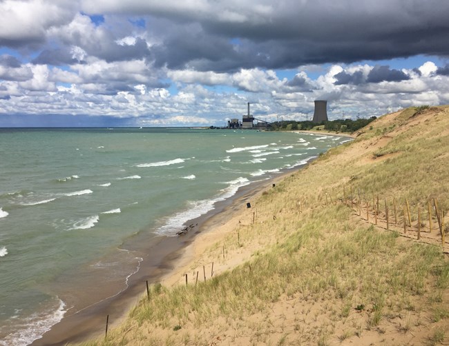 Grass covered dune overlooking a tumultuous Lake Michigan with a power plant in the background.