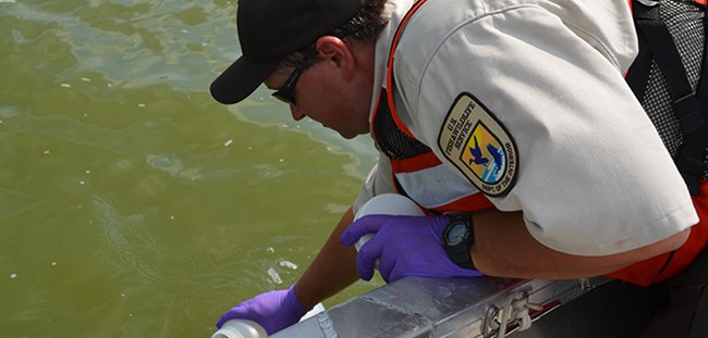 A Fish and Wildlife Service male biologist collects a water sample from a boat.
