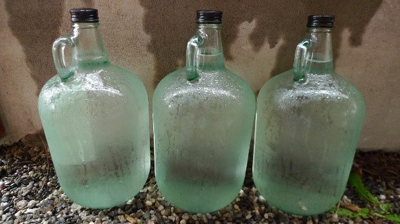 Three glass, gallon sized bottles filled with a clear liquid.