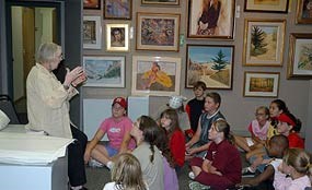 Artist standing in front of kids sitting on the floor of an art gallery