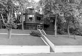 three story house on a small wooded hill with stairs going up to it