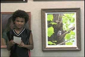 a young boy standing next to painting of a samll owl sitting in a tree