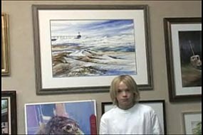 boy standing in front of a painting of a lighthouse with waves crashing around it.