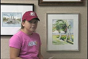 Girl sitting next to a painting of palm trees by a beach