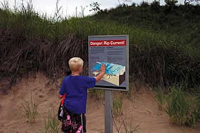 boy standing in front of a sign during the summer that talks about rip currents