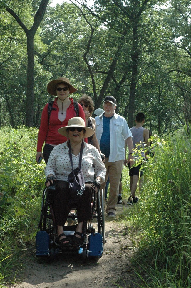 Woman riding wheelchair equipment with group of people following her.