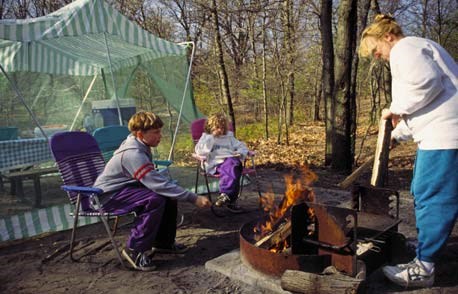 A family getting a fire started at a camp site.
