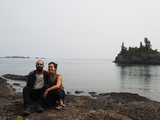 two persons sitting on a rock outcropping, elevated above Lake Superior