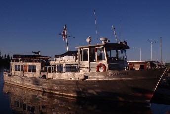 A metal boat with Voyageur II on the side rests at a dock on a sunny day
