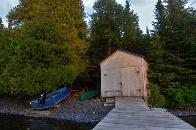 wooden boathouse with a canoe at left and a small motorboat further left