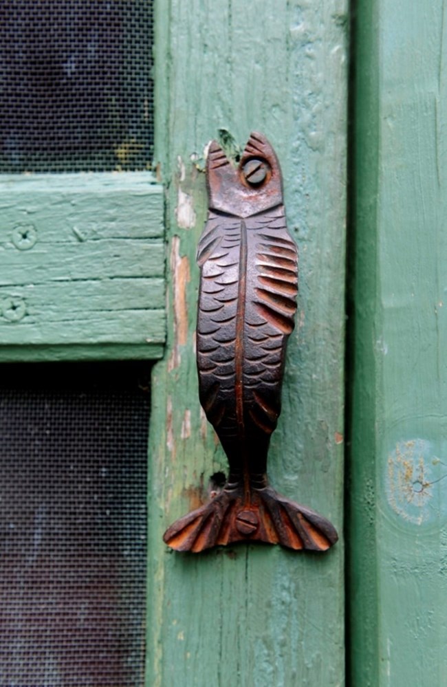 metal door handle shaped like a fish, mounted on a green door