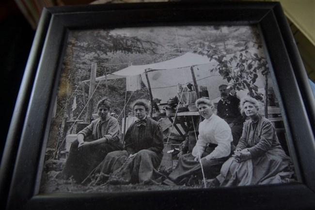 framed black and white photo pf four persons sitting in a fishing camp