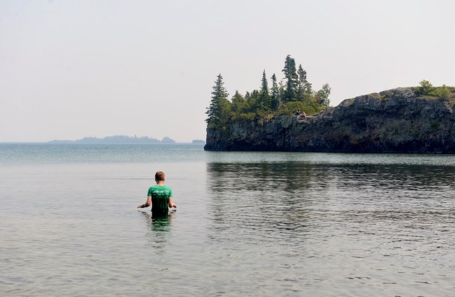 child wading in lake, rock outcropping farther back