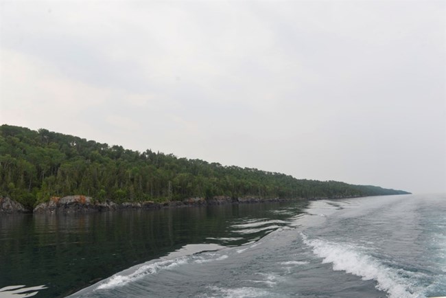 wake behind a boat with rocky, tree covered shoreline