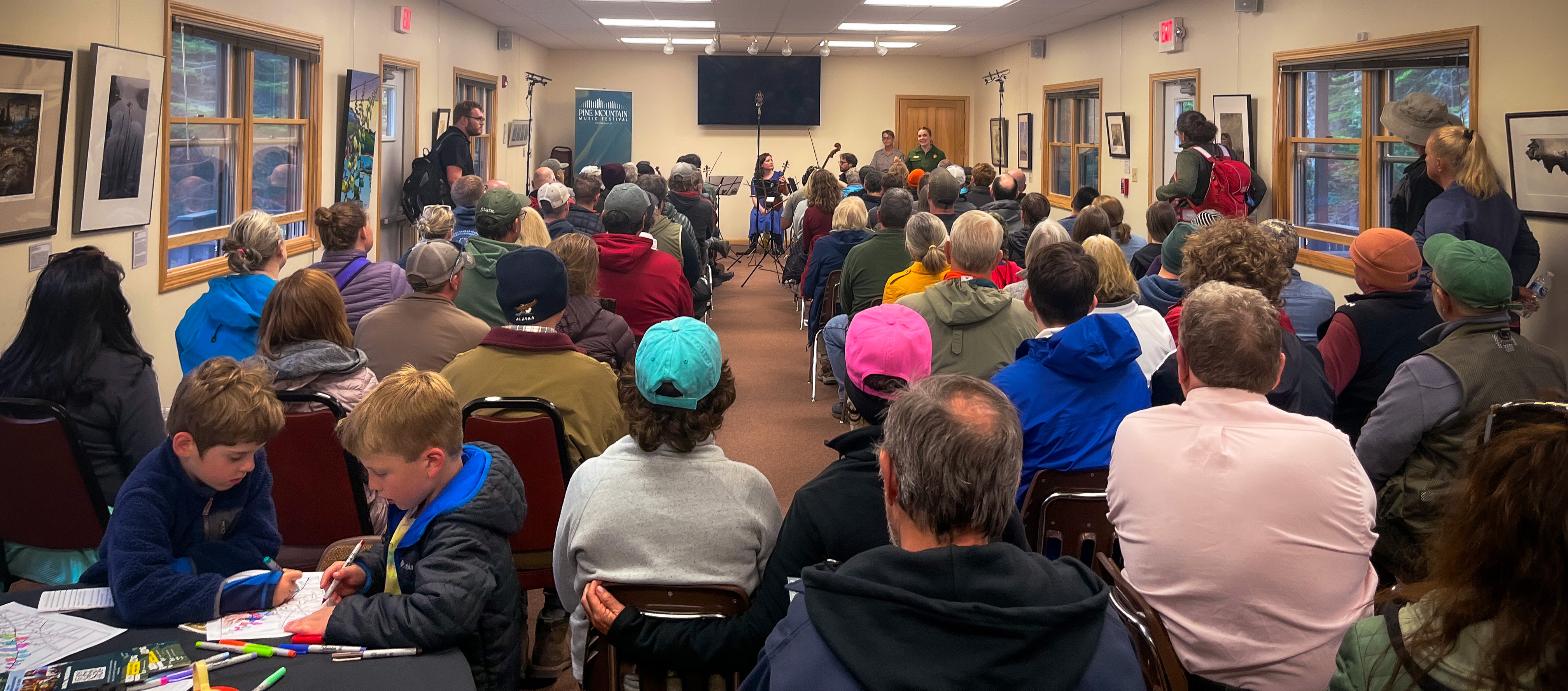 large audience seated and listening to music, children coloring in the foreground
