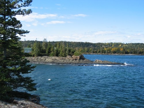 A cove with a rocky peninsula has a small cabin on it, to the right is open lake