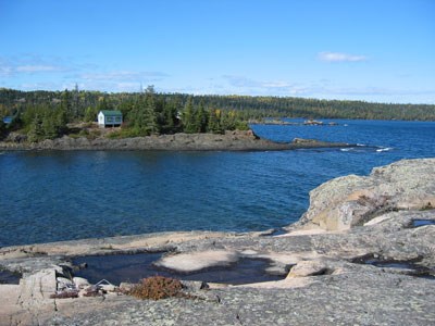 The Dassler Cabin sits hidden amongst trees while its nearby smaller Guest House perches on the shoreline. Viewed from Scoville Point across a bay.