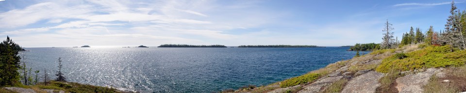 A panoramic image shows distant islands from a rocky shore on a clear day
