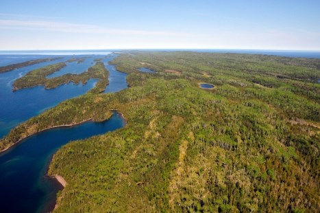 An aerial photo shows a green, lush island surrounded by rich blue water. Lots of long, thin pieces of land are off to the left